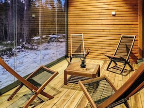 Una terraza de madera con dos sillas y una mesa, con vista a un paisaje nevado.