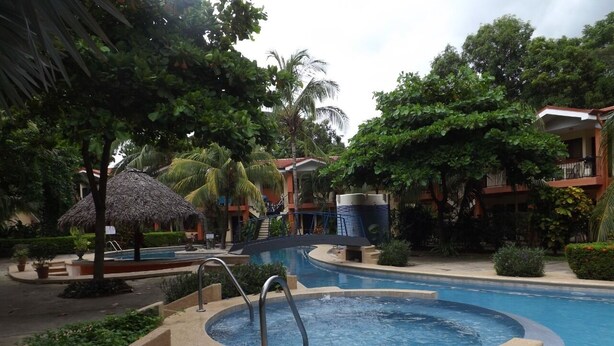 Zwembadgedeelte van een resort met een jacuzzi, palmbomen en een gebouw met balkons op de achtergrond.