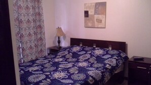 Een kamer met een bed, nachtkastje, lamp en een kunstwerk aan de muur.