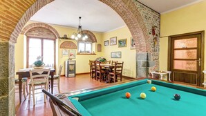 Een biljartkamer met een pooltafel, stoelen, een eetgedeelte met een tafel en stoelen, en een bakstenen boog.