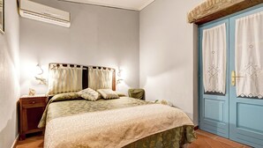 Een slaapkamer met een bed, nachtkastje, lamp en een blauwe deur.