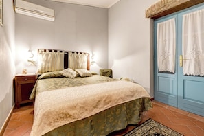 A bedroom with a bed, nightstand, lamp, and a blue door. - Luxury Villa In Cortona (Cortona)