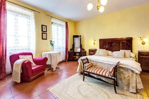 A bedroom with a bed, a chair, a small table, and a mirror.