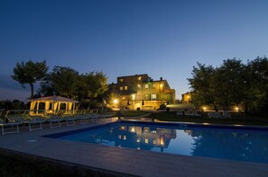 A swimming pool with lounge chairs, a gazebo, and a large building with multiple windows and lights. - Luxury Villa In Cortona (Cortona)