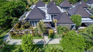 A residential area with multiple houses featuring dark roofs and a well-maintained garden with various plants and a pathway. - Room-kori Maharani Villas - One-bedroom (Gianyar)
