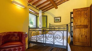 A bedroom with a metal bed frame, a red leather chair, a wooden door, and a bookshelf. - Villa con Piscina, Sauna, Jacuzzi (Greve in Chianti)