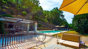 A poolside area with a stone barbecue, outdoor seating, and a view of a natural hillside. - Villa con Piscina, Sauna, Jacuzzi (Greve in Chianti)