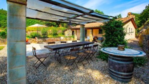 An outdoor patio with a table and chairs, a pergola, and a stone building in the background. - Villa con Piscina, Sauna, Jacuzzi (Greve in Chianti)