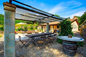 An outdoor patio with a table and chairs, a pergola, and a stone building in the background.