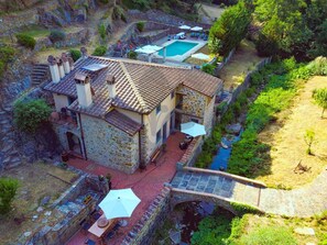 A stone house with a swimming pool, outdoor seating, and a bridge over a stream.
