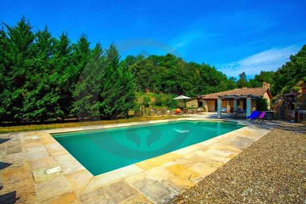 A rectangular swimming pool with stone tiles, surrounded by a stone deck.