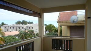 A balcony with a table and chairs, a satellite dish, and a view of neighboring buildings and greenery. - Residence La Colombe Vacation Rentals (Mont Choisy)