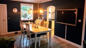 Un comedor con una mesa y sillas, un ventanal con plantas, una cocina al fondo y un televisor montado en la pared.