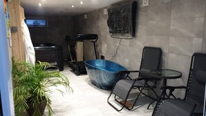 A bathroom with a large blue bathtub, exercise equipment, a small table, and a potted plant. - Private Hot Tub, Sauna, Ice Bath Gym Apartment (Rainham)