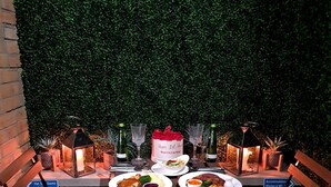An outdoor dining area with a table set for two, surrounded by greenery and illuminated by lanterns. - Private Hot Tub, Sauna, Ice Bath Gym Apartment (Rainham)