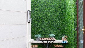 A door with a keypad lock, a small table with chairs, and a green hedge wall. - Private Hot Tub, Sauna, Ice Bath Gym Apartment (Rainham)
