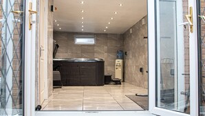 A modern bathroom with a glass shower enclosure, a built-in bathtub, and a water heater. - Private Hot Tub, Sauna, Ice Bath Gym Apartment (Rainham)