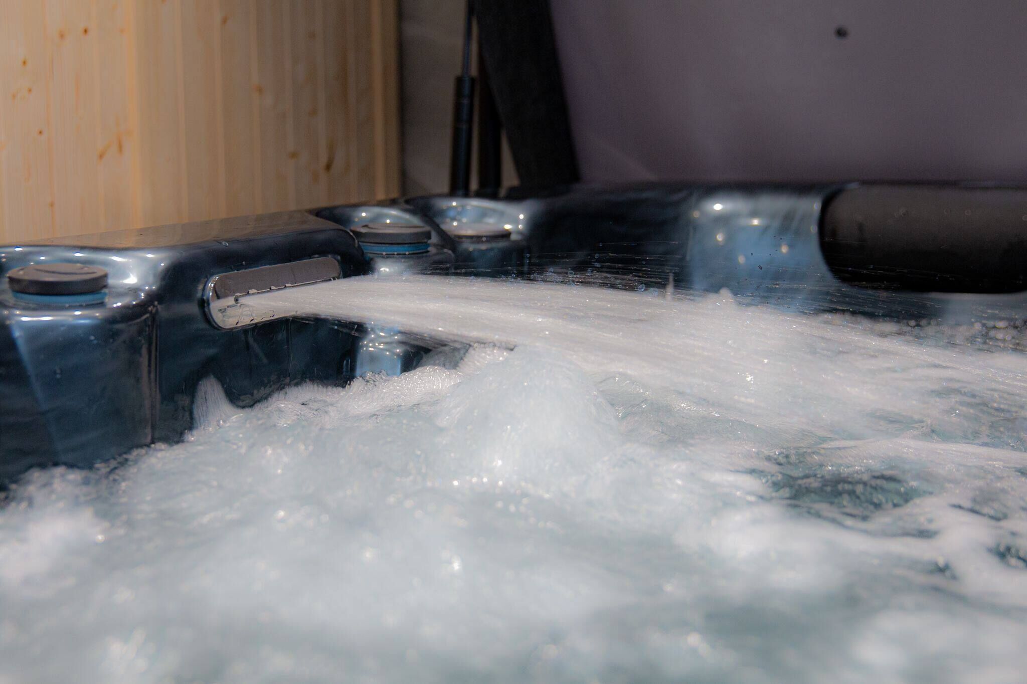 A hot tub with water flowing out, surrounded by a wooden wall and a metal structure.