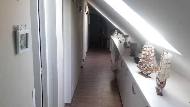 Un couloir étroit doté d’un plancher en bois, de murs blancs et d’une lucarne.