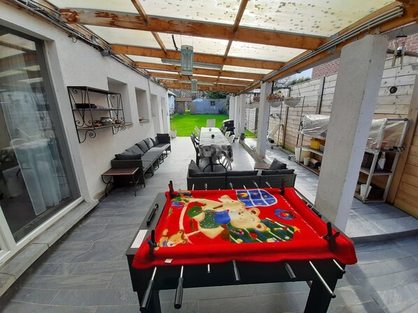 An outdoor patio with a pool table, seating area, and a covered walkway.