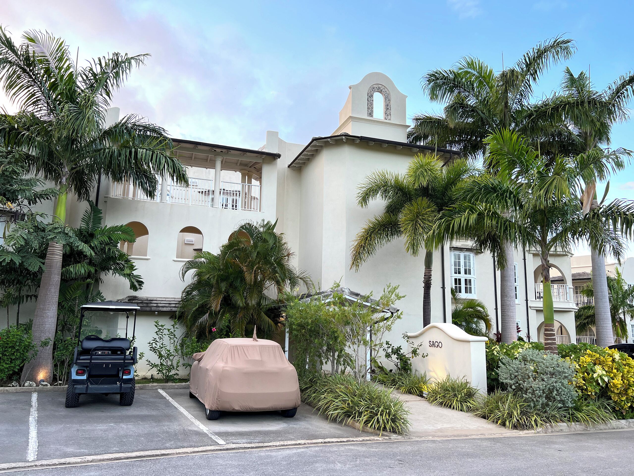 A covered car in a parking lot, a building with a bell tower, and palm trees.