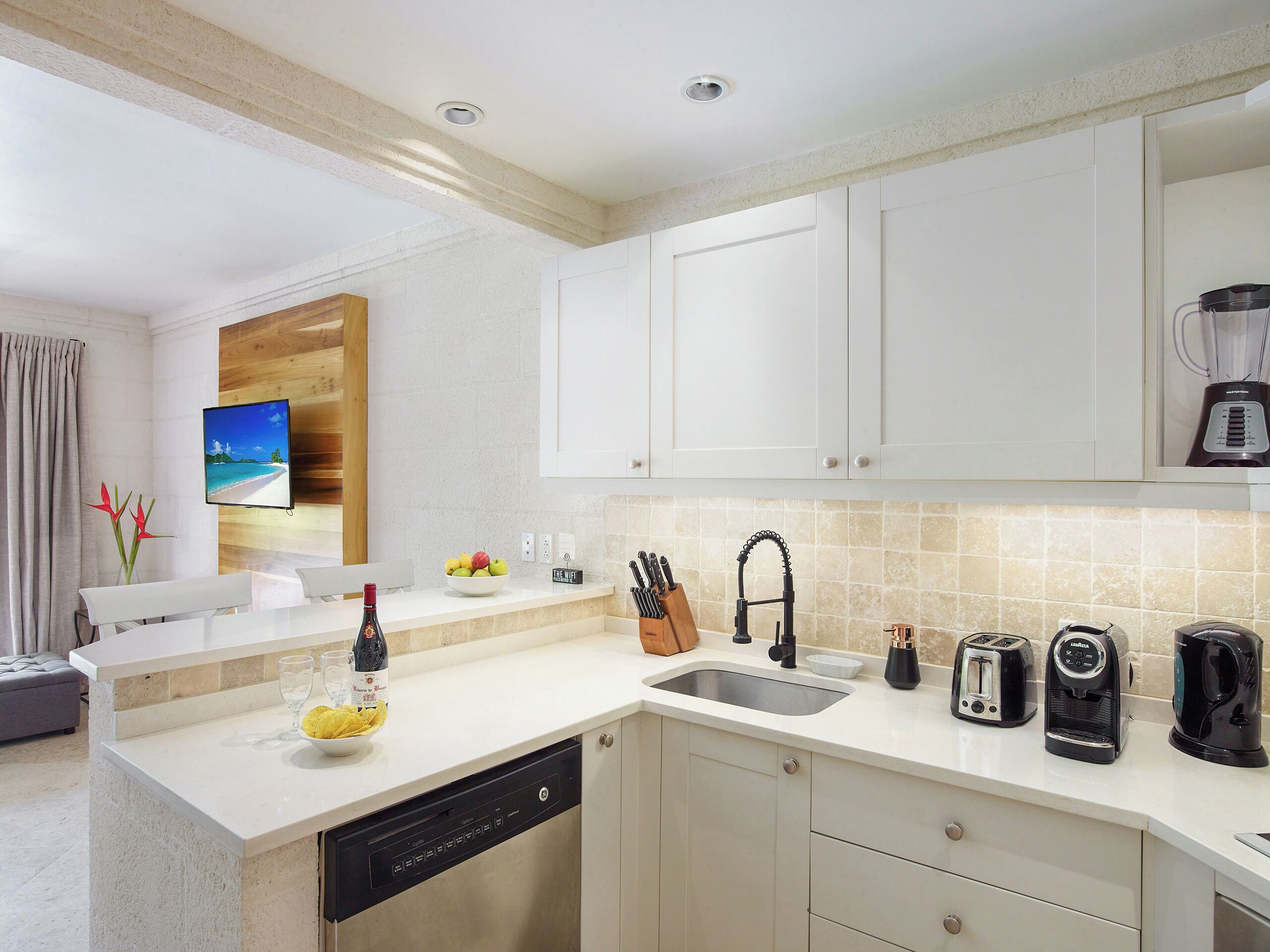 Una cocina moderna con muebles blancos, lavavajillas integrado, un fregadero y una cafetera.