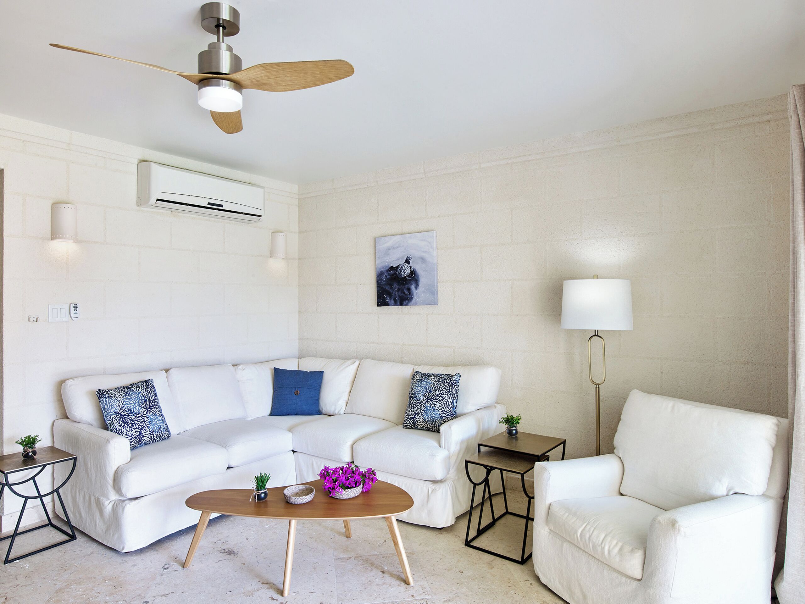 A living room with a white sectional sofa, a wooden coffee table, a floor lamp, and a ceiling fan.