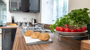 Una cocina con encimera de madera, tabla de cortar con pan, un lavamanos y una ventana con vistas a árboles.