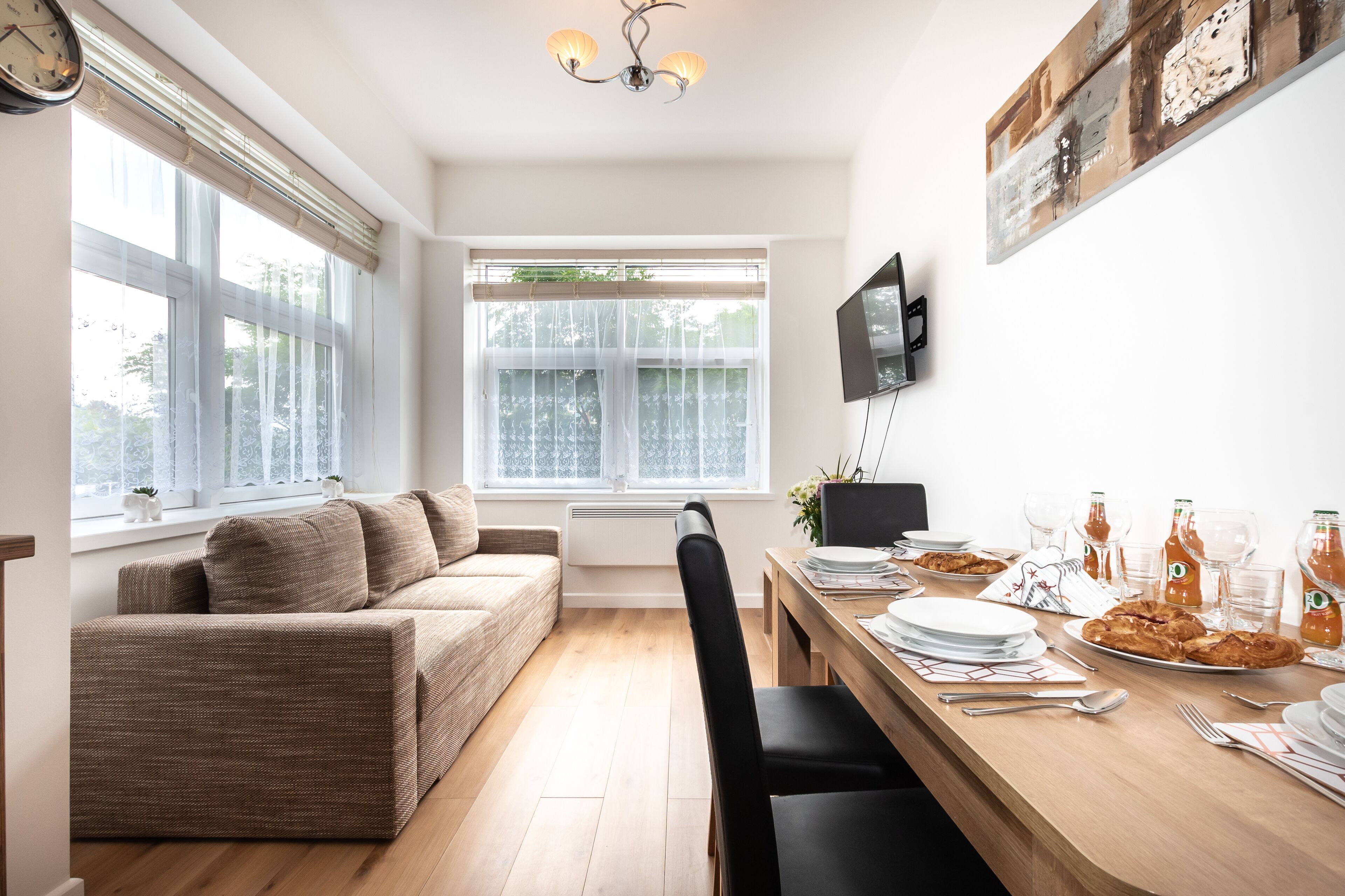 Zona pranzo moderna con tavolo in legno apparecchiato per un pasto, un divano e una TV montata a parete.