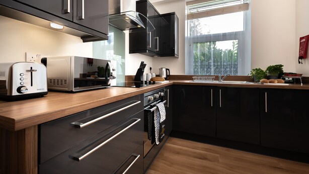 Una cocina moderna con gabinetes negros, electrodomésticos de acero inoxidable y encimera de madera.