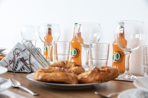 Una colazione con croissant, bicchieri e bottiglie di succo d'arancia su un tavolo di legno.