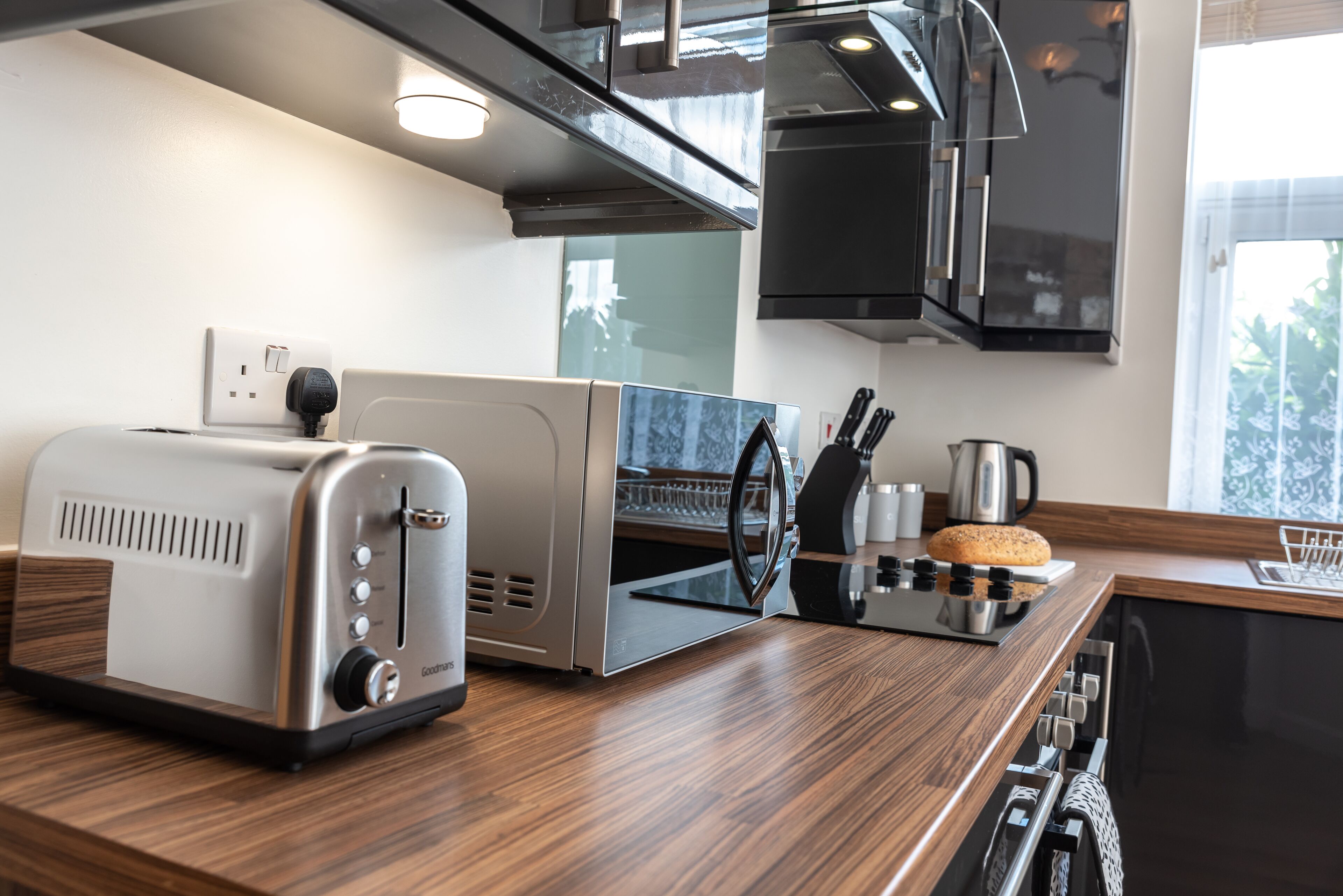 Une cuisine moderne équipée d’un grille-pain, d’un appareil à griller le pain, d’une bouilloire et d’une machine à café, le tout posé sur le plan de travail.