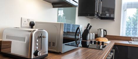 Une cuisine moderne équipée d’un grille-pain, d’un appareil à griller le pain, d’une bouilloire et d’une machine à café, le tout posé sur le plan de travail.