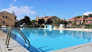 A swimming pool with a metal ladder, surrounded by buildings with red roofs and a clear blue sky. - Terraced House With Private Garden (San Michele al Tagliamento)
