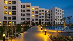 Ett modernt hotell med flera vita byggnader, en central pool och väl upplysta gångvägar.