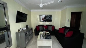 A living room with a flat-screen TV, a ceiling fan, a sofa with red and black cushions, a coffee table, and a cabinet. - Entire Apartment Tu Nido De Amor #2 Santo Domingo West (Santo Domingo)