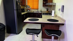 A compact kitchen with a refrigerator, stove, sink, and two bar stools. - Entire Apartment Tu Nido De Amor #2 Santo Domingo West (Santo Domingo)