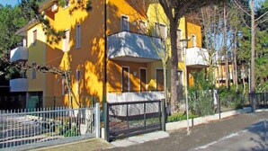 A yellow building with a balcony, surrounded by trees and a fence. - Modern Apartment in a Quiet Area (San Michele al Tagliamento)