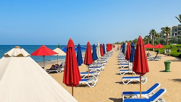 Ein Strand mit Reihen von Liegestühlen und Sonnenschirmen, einem klaren Himmel und ruhiger See.
