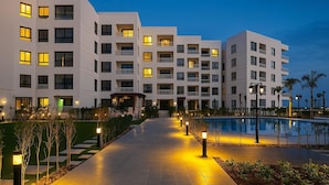 Ein modernes Hotel mit mehreren weißen Gebäuden, einem zentralen Pool und gut beleuchteten Wegen.