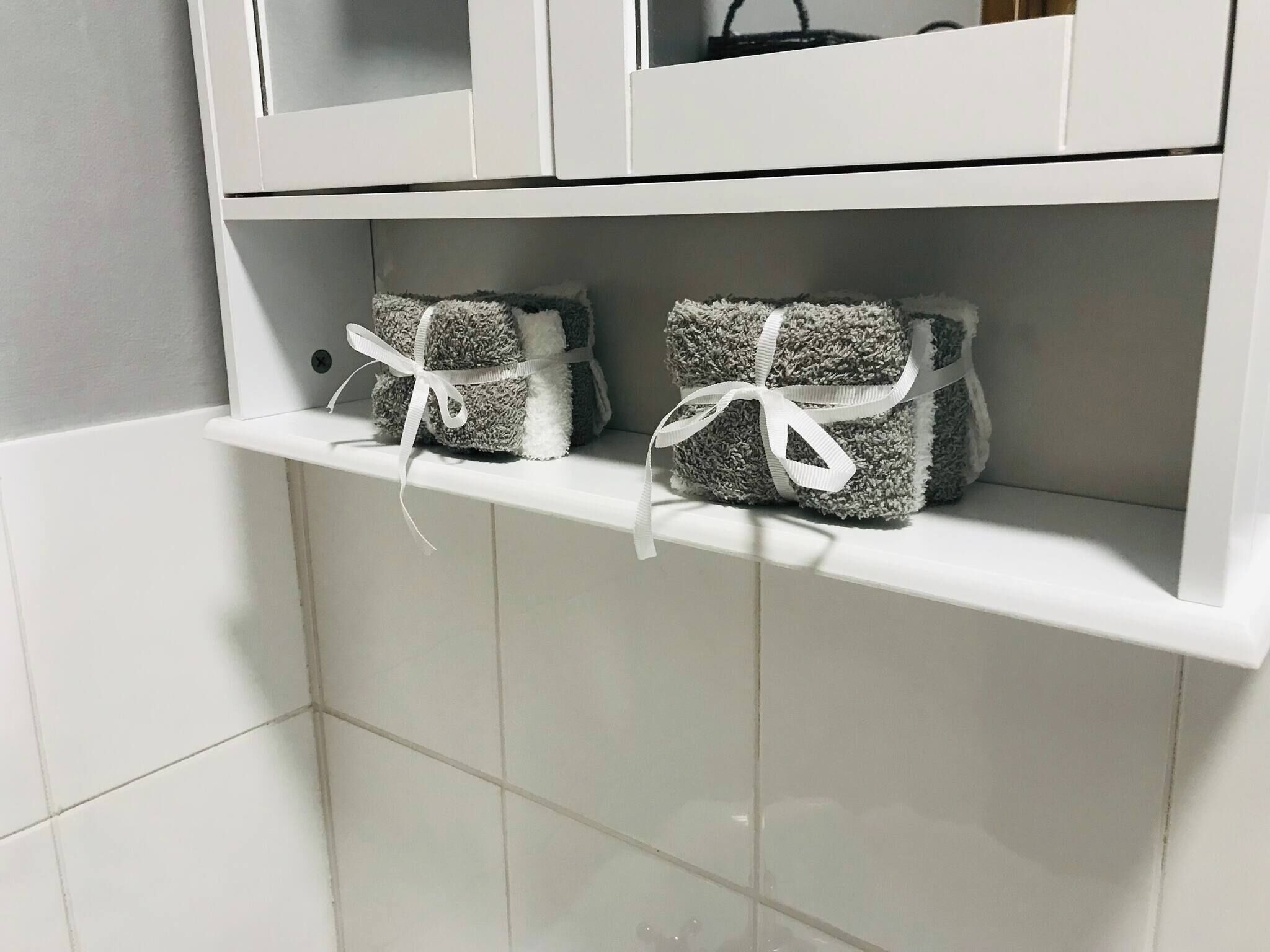 A white tiled bathroom with a shelf holding two white towels tied with ribbons.