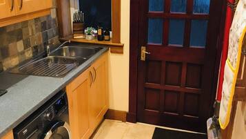 Une cuisine compacte équipée d’un lave-linge, d’un évier, de meubles en bois, d’une fenêtre et d’une porte avec des panneaux de verre.