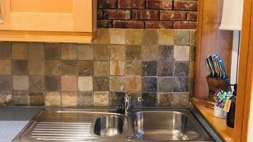 A kitchen with a stainless steel sink, wooden cabinets, a tiled backsplash, and a brick wall.
