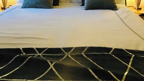A neatly made bed with a white duvet and two pillows, flanked by two bedside lamps. Above the bed, there are three wall-mounted decorative panels. - Station View Lodge - Near Balbirnie House Markinch (Glenrothes)