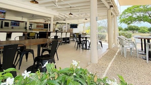 Un café al aire libre con mesas y sillas, una zona de bar y vistas del paisaje circundante.