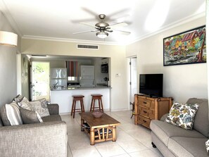 A living room with a sofa, a coffee table, a TV, and a kitchen area in the background.