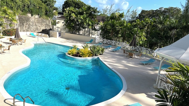 Una piscina con una pequeña cascada, rodeada de sillones de descanso y un área de estar cubierta.