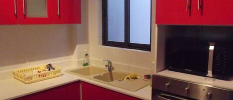 Et køkken med røde skabe, en vask, et vindue og en mikroovn.