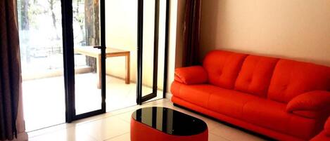 Una sala de estar con un sofá rojo, una mesa de centro negra y un ventanal corredero que da a un espacio exterior.