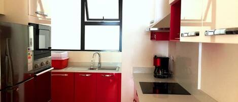 A compact kitchen with a microwave, stove, sink, and red cabinets.